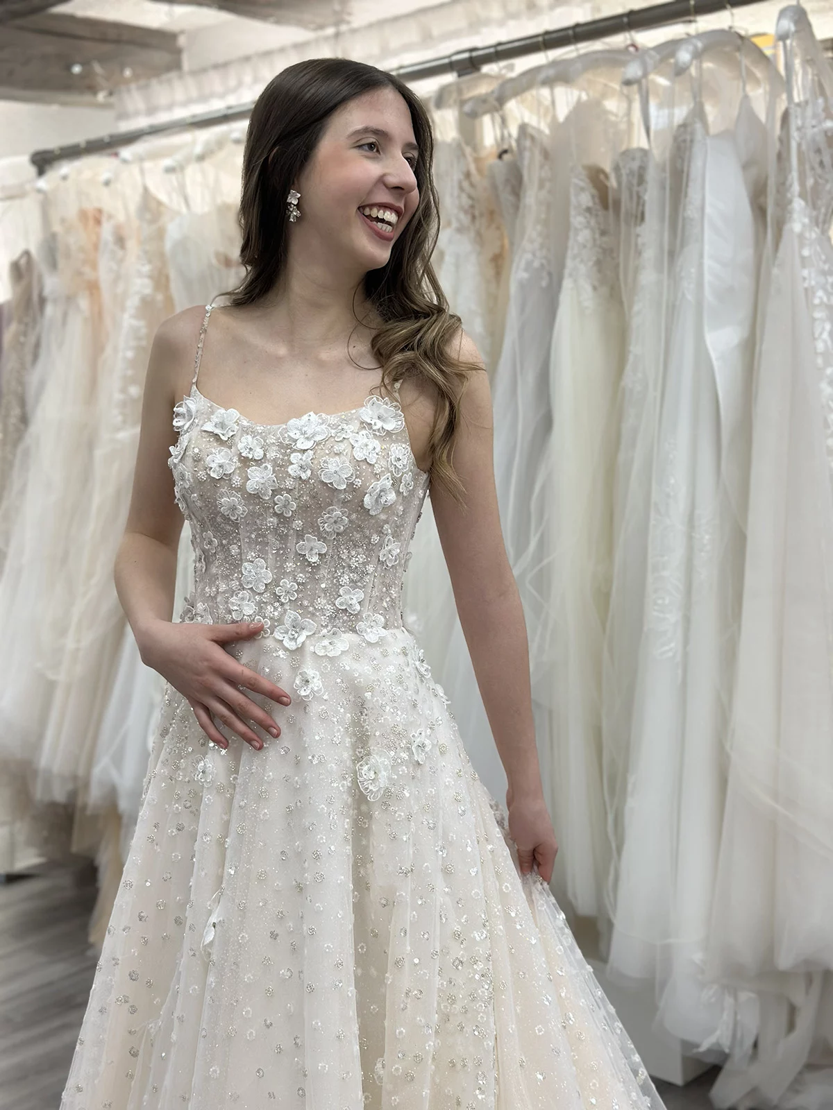Eine lachende Frau trägt ein mit Blumen besticktes Brautkleid in einem Brautmodengeschäft.