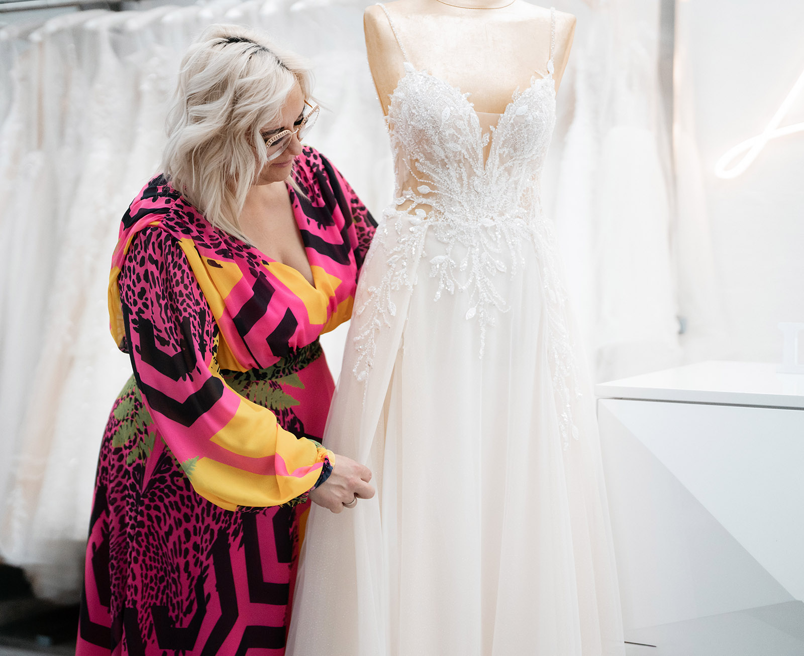 Person in buntem Kleid bedient Mannequin mit weißem Brautkleid, fokussiert im Geschäftsumfeld.