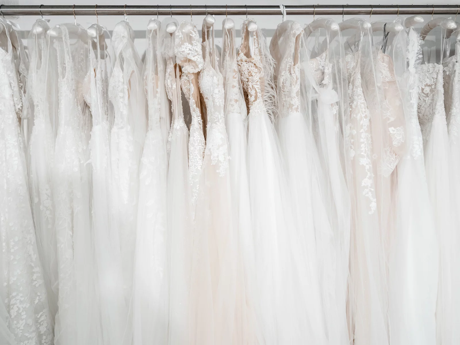 Weiße und cremefarbene Brautkleider hängen dicht nebeneinander an einer Kleiderstange.